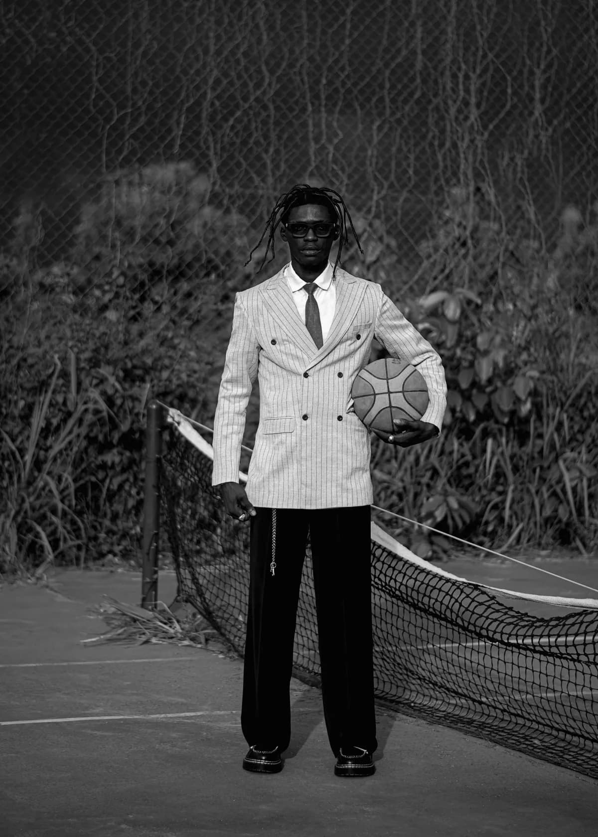Man in a striped double-breasted blazer and wide black trousers holding a basketball on a court
